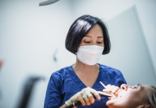 Dr. Sonja Tai in blauer Arbeitskleidung und Maske bei einer zahnärztlichen Behandlung.